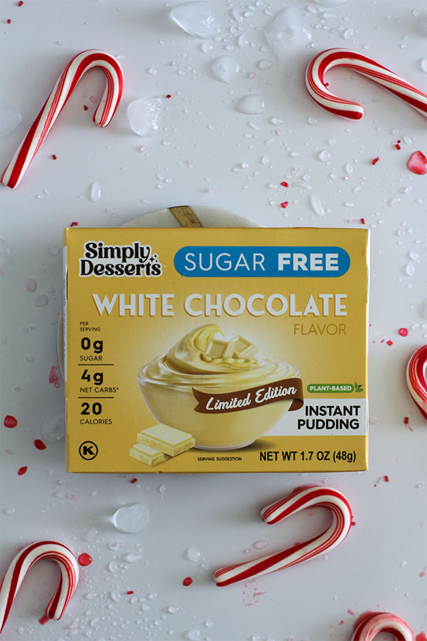 Simply Desserts Sugar Free White Chocolate Pudding box surrounded by candy canes and ice on a festive white background