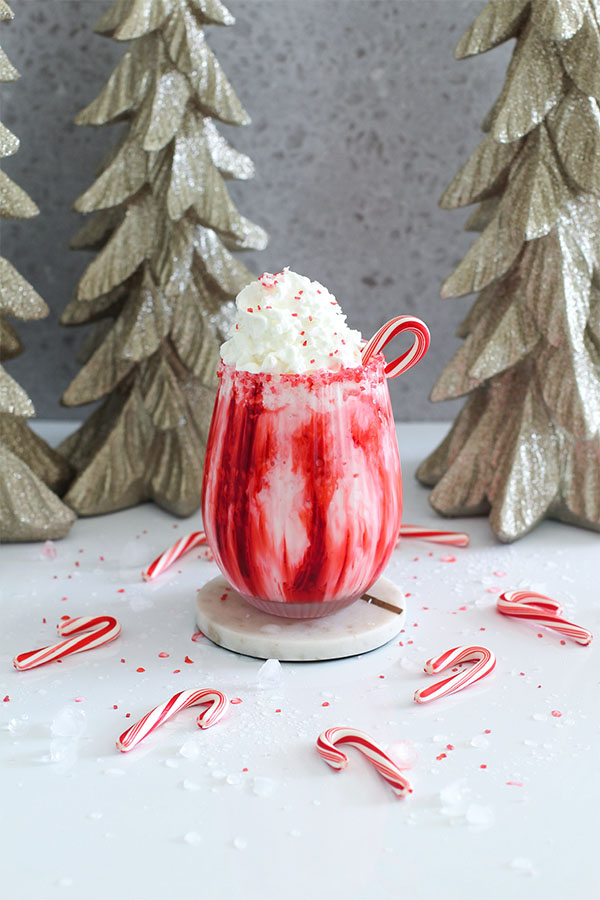 Holiday-themed peppermint mocktail with red swirl effect and whipped cream garnish, surrounded by candy canes and glittery Christmas trees