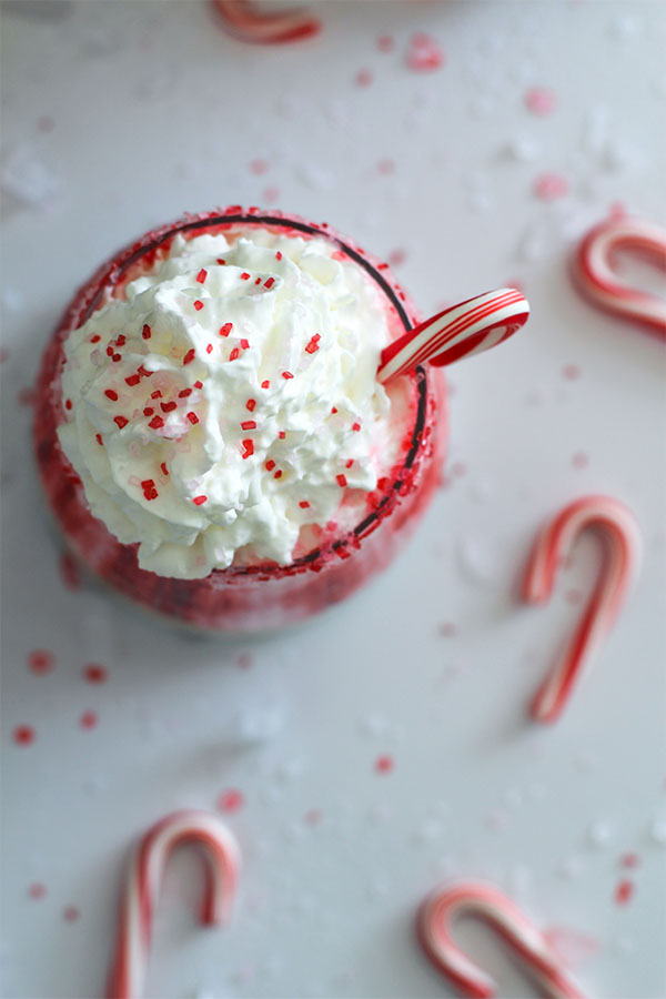 Top view of the Candy Cane Lane Mocktail with whipped cream, red sprinkles, and a mini candy cane in a rimmed glass