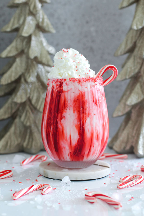 Front view of a creamy peppermint mocktail in a red and white swirl glass, garnished with whipped cream and candy cane, set against festive holiday decor