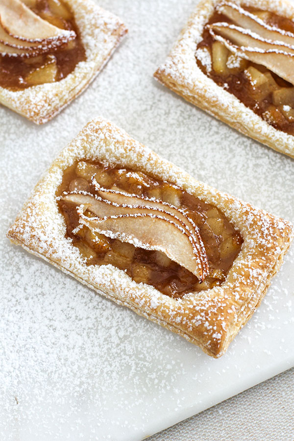 A top-down view of golden brown pear puff pastry tarts with fanned pear slices, lightly dusted with powdered sugar