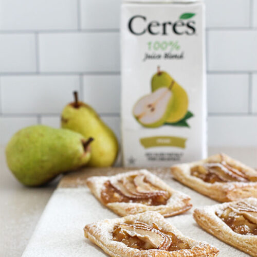 A close-up of multiple pear puff pastry tarts on a marble board, highlighting the golden crust, pear slices, and powdered sugar topping