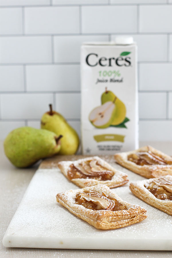 A close-up of multiple pear puff pastry tarts on a marble board, highlighting the golden crust, pear slices, and powdered sugar topping