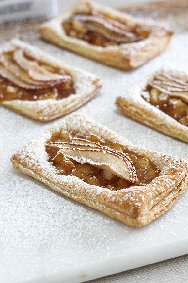 A close-up side view of pear puff pastry tarts, showing the crispy, flaky layers of the pastry topped with caramelized pears