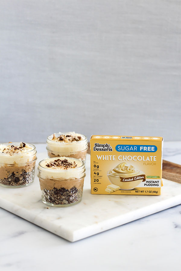 Simply Desserts Sugar-Free White Chocolate Pudding box displayed next to prepared White Chocolate Caramel Wafer Gu Pots on a marble surface