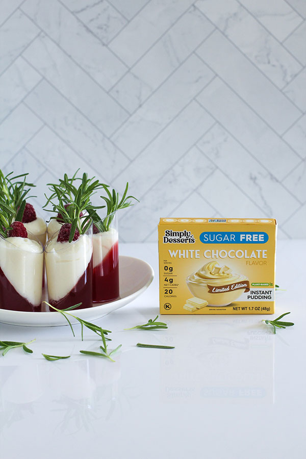 Simply Desserts Sugar Free White Chocolate Pudding box next to a plate of white chocolate cranberry passionfruit shooters, arranged with rosemary sprigs for decoration