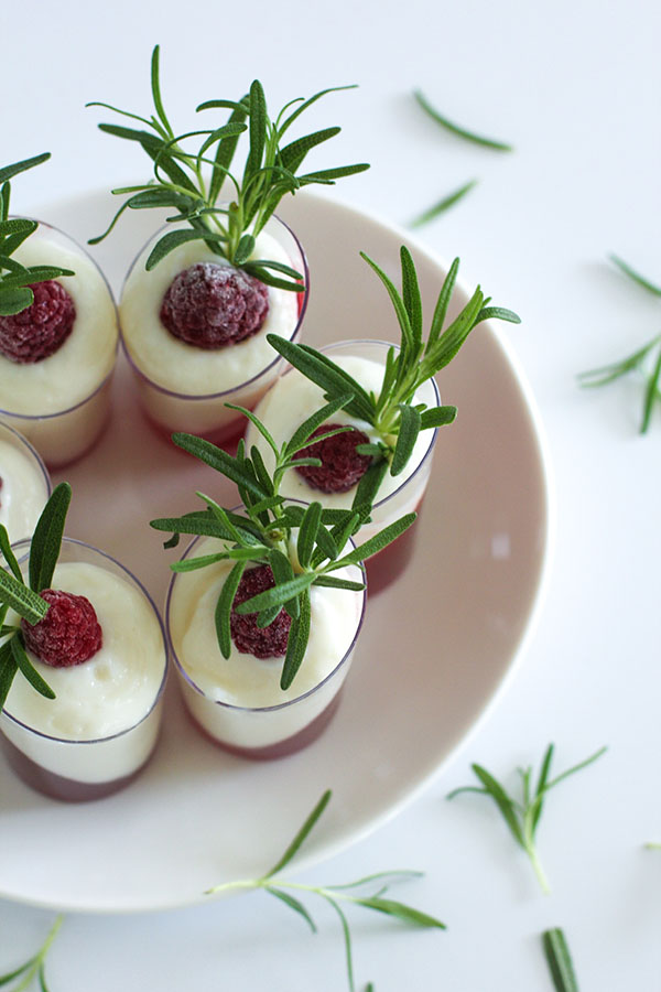Top-down view of multiple white chocolate cranberry passionfruit shooters on a plate, beautifully garnished with rosemary and raspberries