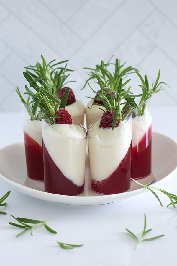 Close-up of a set of white chocolate cranberry passionfruit shooters, featuring a smooth layered effect and fresh garnishes