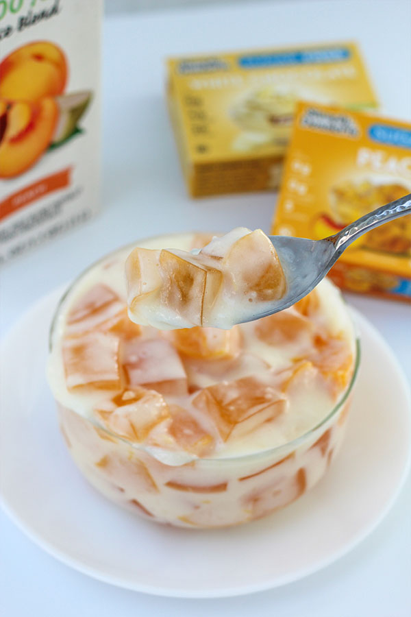Peach jel cubes and white chocolate pudding on a spoon, above a serving bowl of the dessert