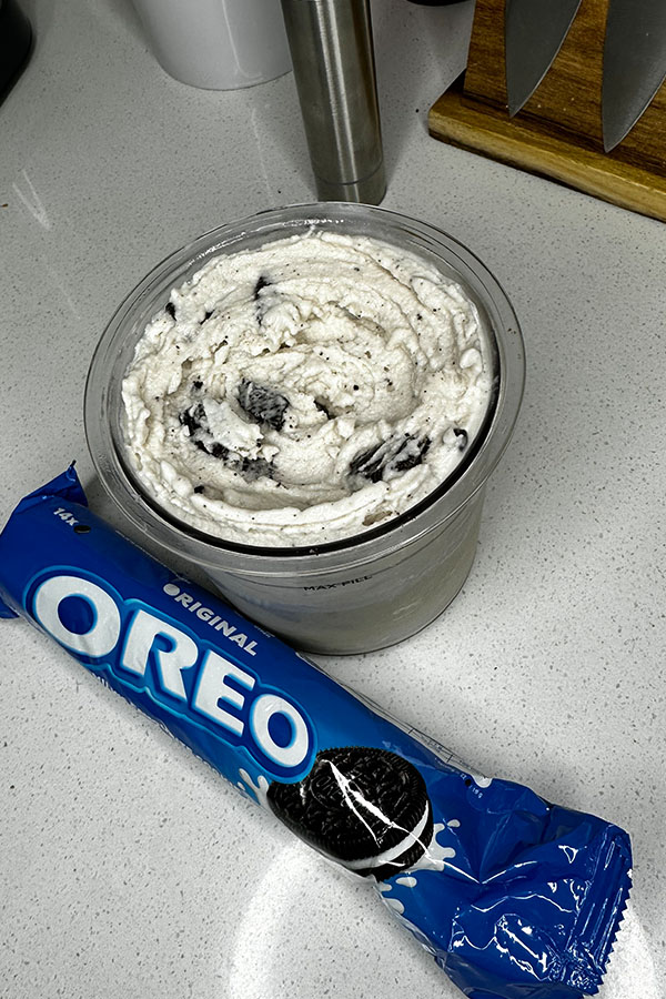 Top view of a Ninja Creami pint filled with cookies and cream ice cream, surrounded by Oreo packaging on a white counter