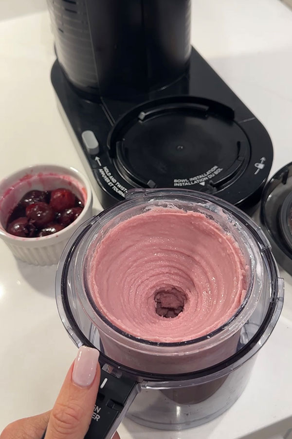 Cherry cheesecake protein ice cream freshly spun in a Ninja Creami container, with a bowl of dark cherries in the background