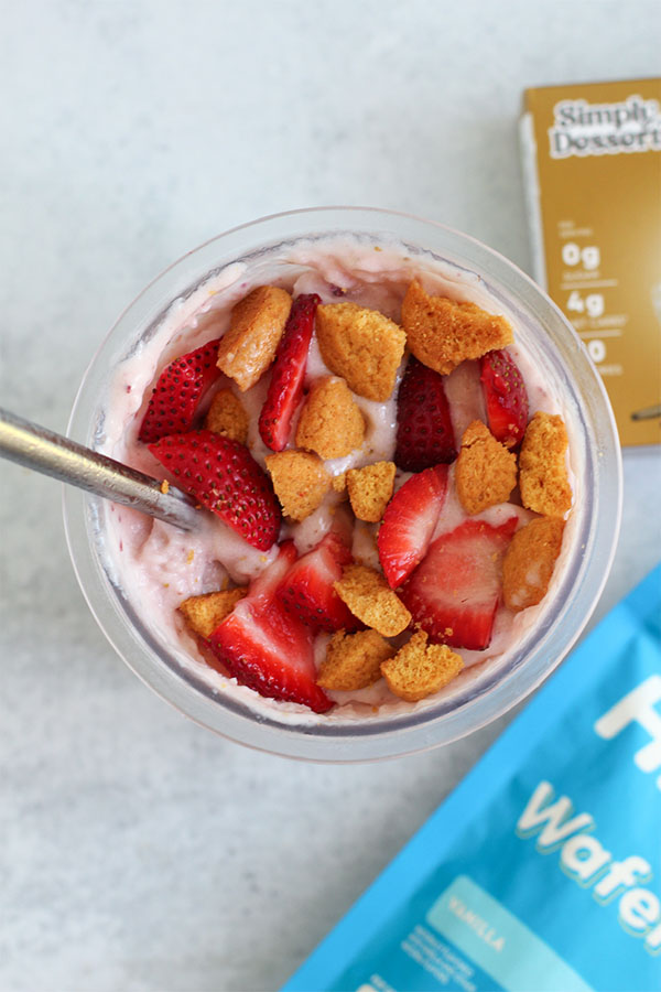 Overhead shot of strawberry shortcake ice cream in a Ninja Creami pint, surrounded by Simply Delish Vanilla Pudding and Highkey Wafers packaging
