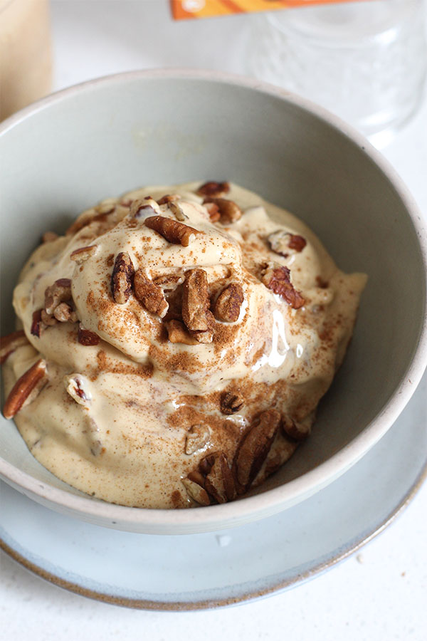 Creamy salted caramel apple pecan crunch ice cream topped with chopped pecans and cinnamon in a ceramic bowl