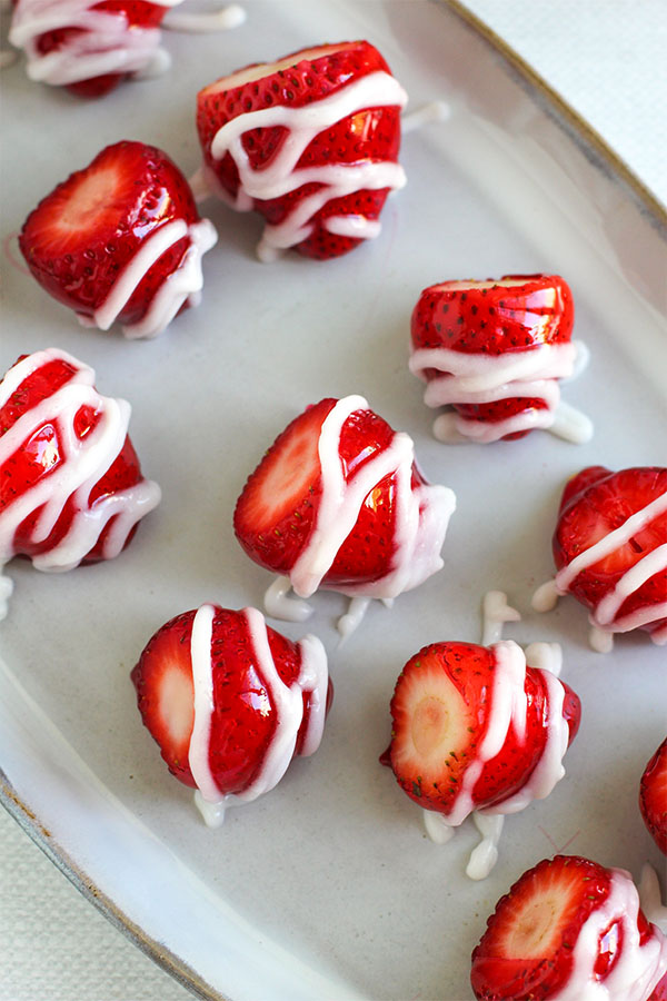 Glossy strawberries with white chocolate drizzle arranged on a plate