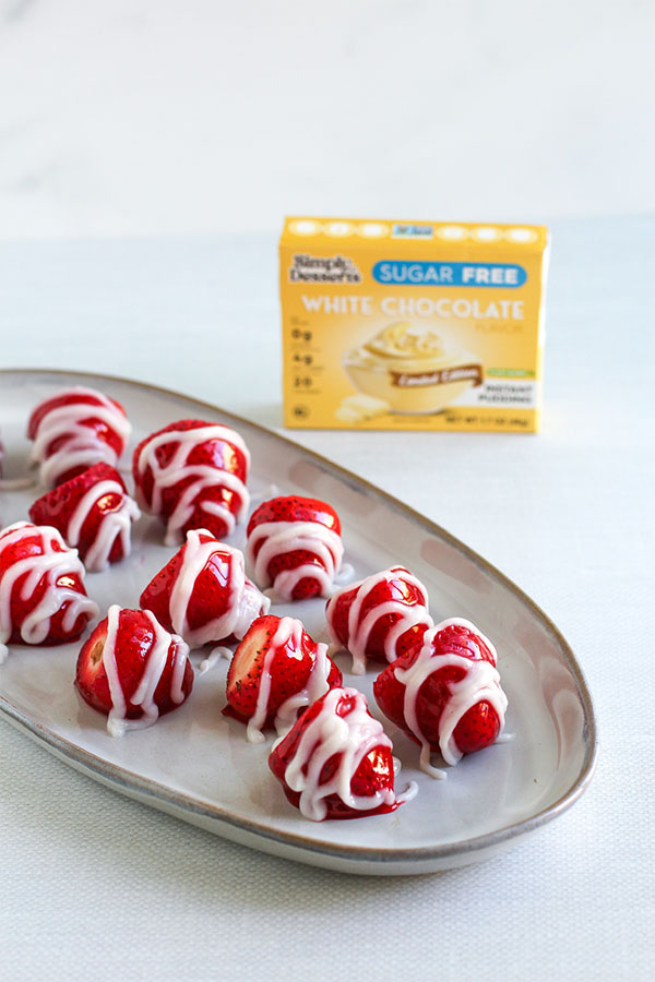 Plate of strawberries drizzled with white chocolate pudding beside Simply Desserts box