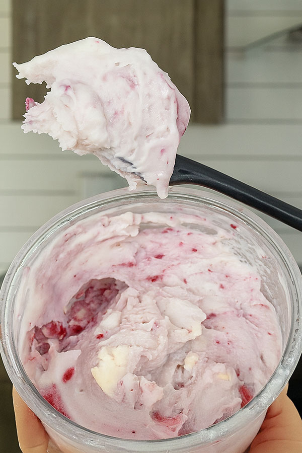 Close-up of homemade white chocolate raspberry cheesecake ice cream with visible raspberry bits and creamy texture in a clear pint container