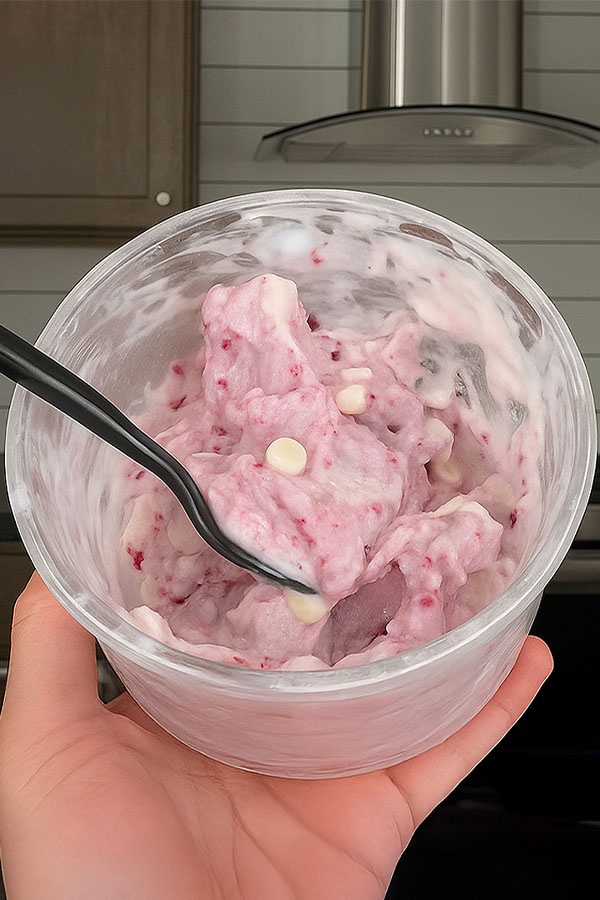 Creamy scoop of white chocolate raspberry cheesecake ice cream showing swirls of raspberry and white chocolate chunks inside a Ninja Creami pint