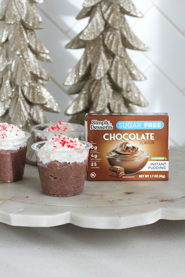 Simply Desserts sugar-free chocolate pudding box beside a festive hot chocolate pudding shot topped with whipped cream and peppermint sprinkles
