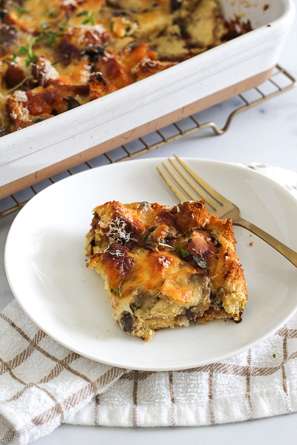 Slice of savory mushroom and cheese bread pudding served on a white plate