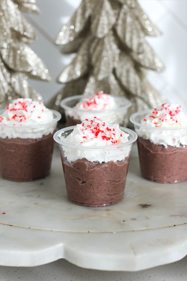 Close-up of sugar-free hot chocolate pudding shots in small cups topped with whipped cream and crushed peppermint sprinkles