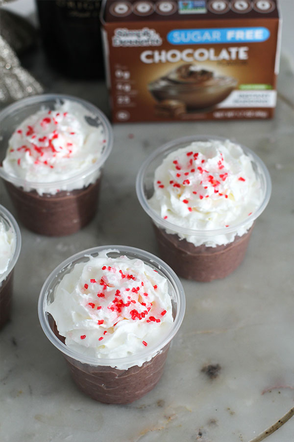 Overhead view of individual hot chocolate pudding shots topped with whipped cream and peppermint sprinkles on a festive serving board