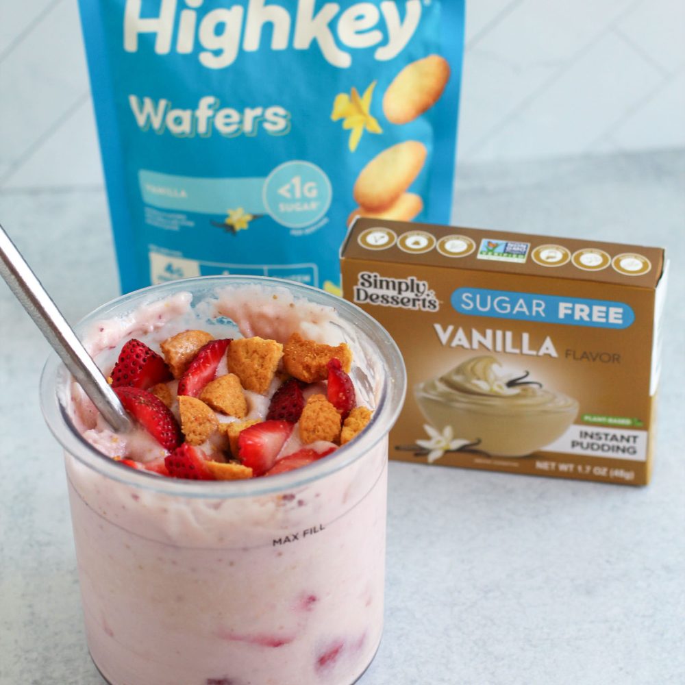 Strawberry shortcake ice cream in a glass bowl with a spoon, placed in front of Simply Delish Vanilla Pudding and Highkey Wafers packaging Featured Image